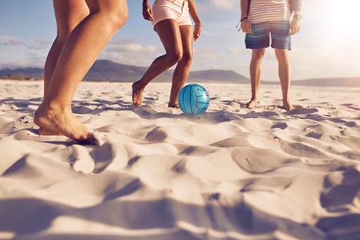 Low section portrait of group of friends playing soccer on the beach. a girl is passing the ball to friends.