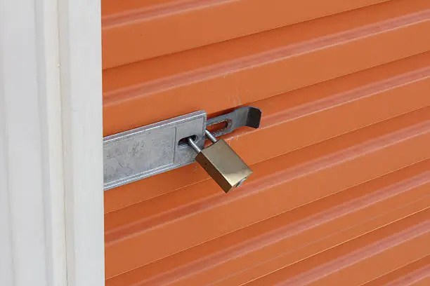 An orange, steel storage door locked with a golden padlock.