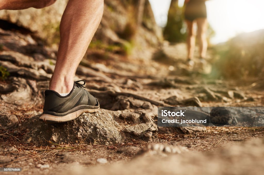 Man trail running on rocky terrain Closeup of man trail running on rocky terrain. Low section of male runner on cross country run. Running Stock Photo