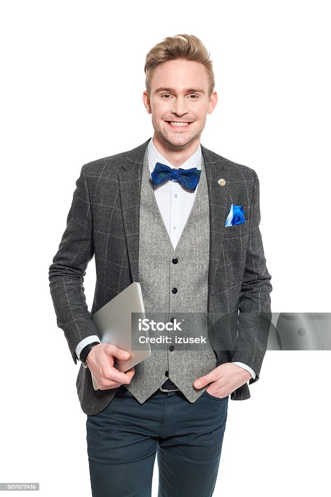 Fashionable young businessman in classical outfit, holding a digital tablet Portrait of fashionable, elegant young businessman wearing tweed jacket and bow tie, holding a digital tablet in hand, smiling at camera. Studio shot, one person, isolated on white. Men Stock Photo