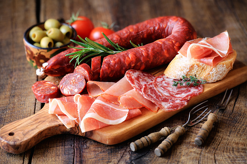 Cured meat platter of traditional Spanish tapas - chorizo, salsichon, jamon serrano, lomo - erved on wooden board with olives and bread