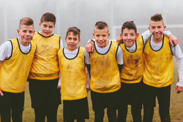 Children playing soccer. Group photo after training or game. Looking at camera and smiling. They are smiling and they are dirty with mud.They are having training with their coach on foggy, cold, winter morning. They are dedicated to become a new soccer stars.