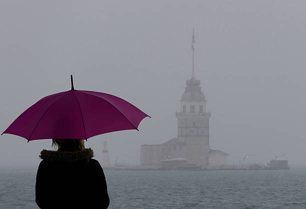 Woman looking at Maiden's Tower Woman with umbrella standing on the beach and looking at Maiden's Tower. maidens tower turkey photos stock pictures, royalty-free photos & images