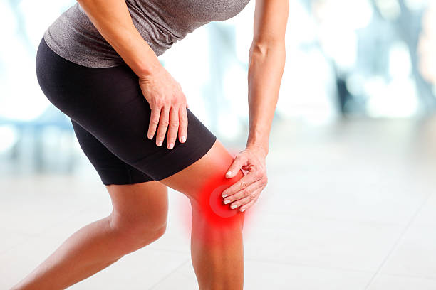 Pain in knee Portrait of sporty woman holding her injured knee after fitness workout. Red colouring spot has been added on the skin to demonstrate where the pain resides. human knee stock pictures, royalty-free photos & images