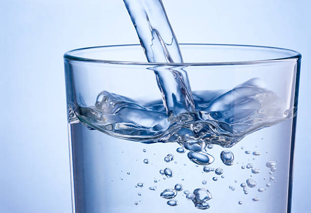 primer plano de agua vertiendo en vidrio sobre fondo azul - agua purificada fotografías e imágenes de stock