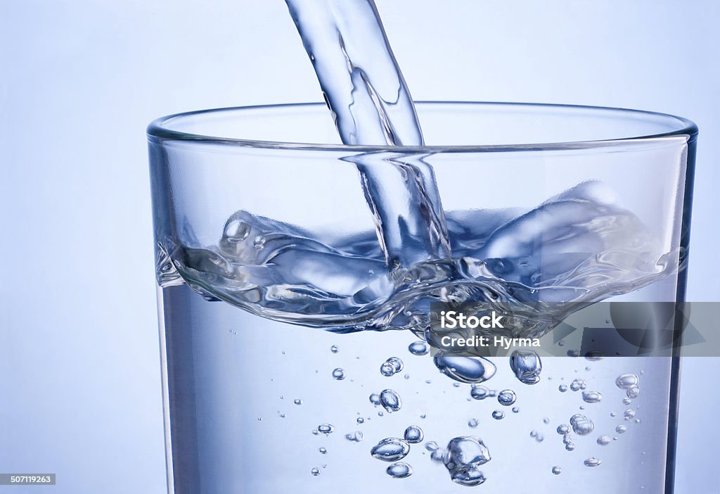 Close-up di versare l'acqua nel bicchiere su sfondo blu - Foto stock royalty-free di Acqua