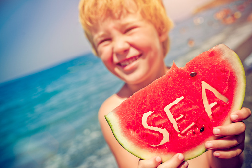 Happy little boy with watermelon on the beach