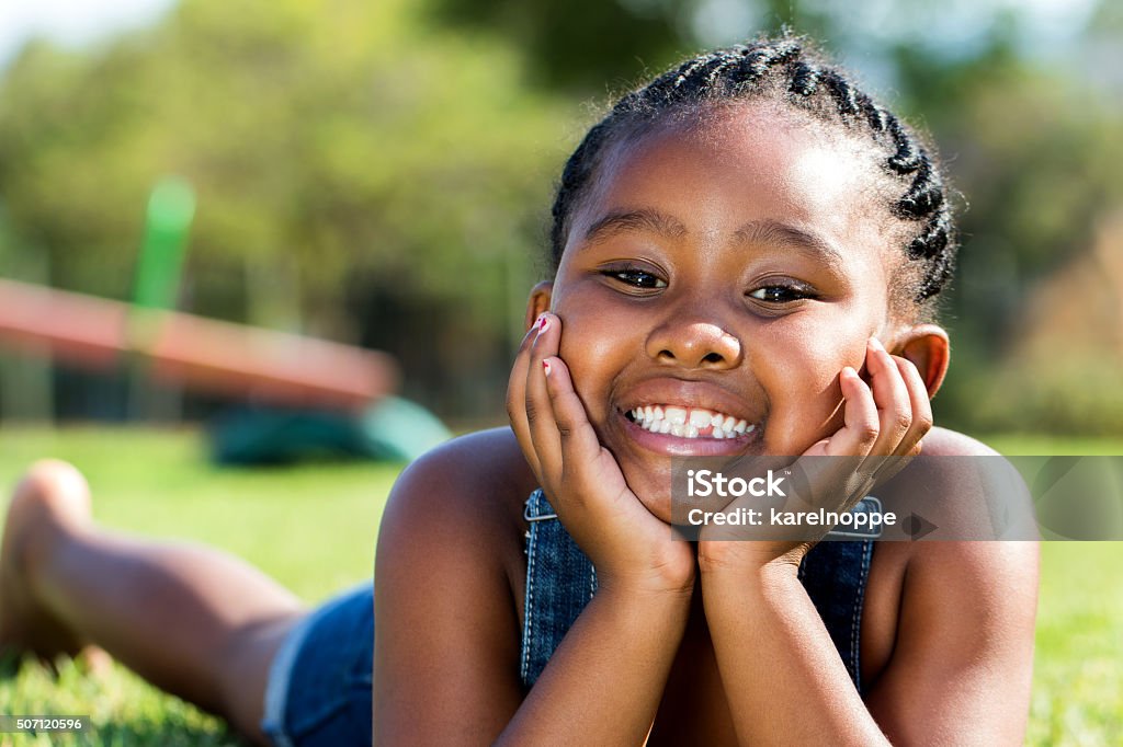 African girl laying with face on hands in park. Close up portrait of cute little African girl laying with face on hands in park. Baby - Human Age Stock Photo