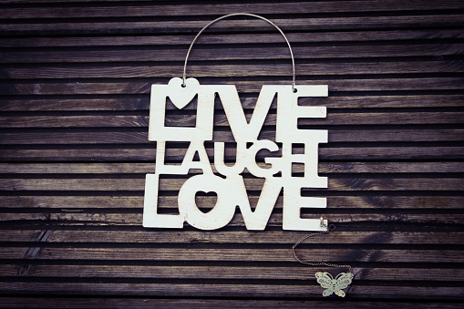 Metal sign with the quote Live Laugh Love with a metal butterfly trinket on a wooden background