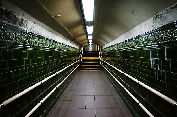 A long straight passageway ending with a staircase in a District Line's underground station.