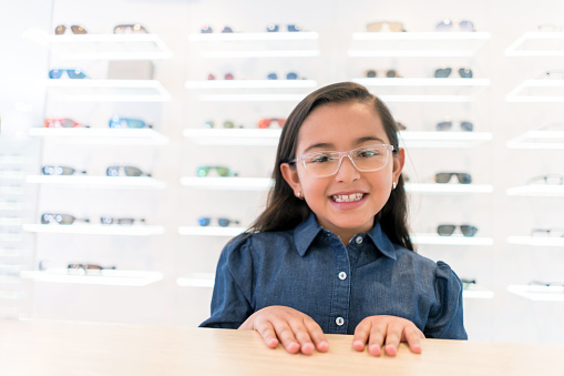 Little girl wearing glasses at the optician's shop - healthcare and medicine concepts