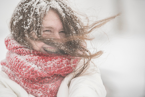 A woman stands on a snowy field with her hands raised up. Panoramic background.