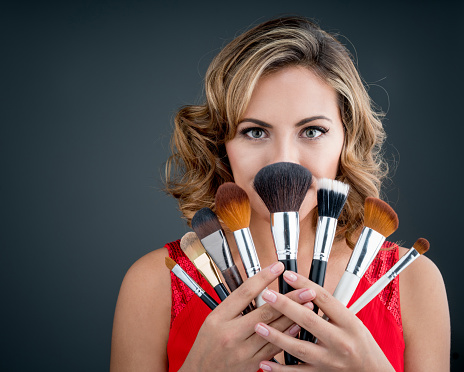 Excited woman holding makeup brushes and covering her face - beauty concepts