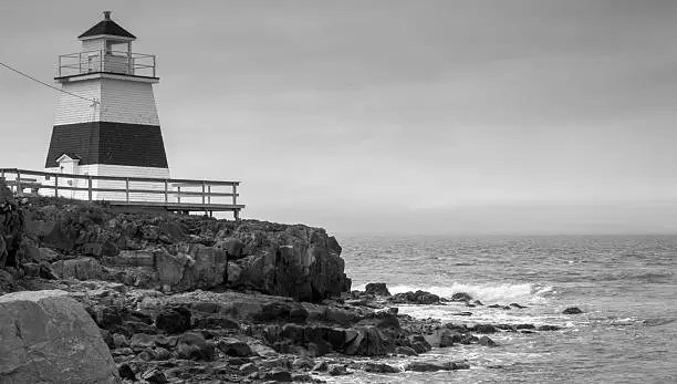 A lone lighthouse atop an outcropping of rock in the Bay of Fundy on an gray sky, late spring day in Nova Scotia.