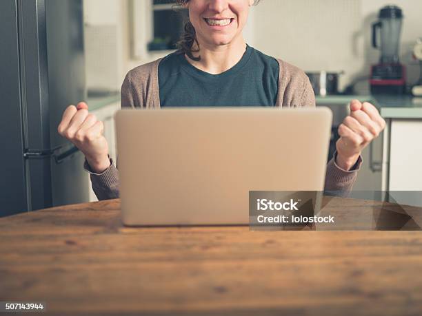 Young Woman With Laptop Fist Pumping In Kitchen Stock Photo - Download Image Now - Achievement, Joy, Adult