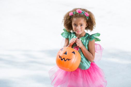 Little girl wearing halloween costume, holding jack o lantern treat bag, ready to go trick or treating. 5 years old, mixed race, African American.