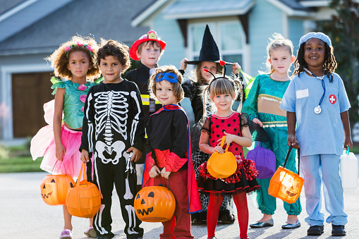 Multi-ethnic group of children 3-6 years old, wearing halloween costumes, ready to go trick or treating, standing in street in front of house.