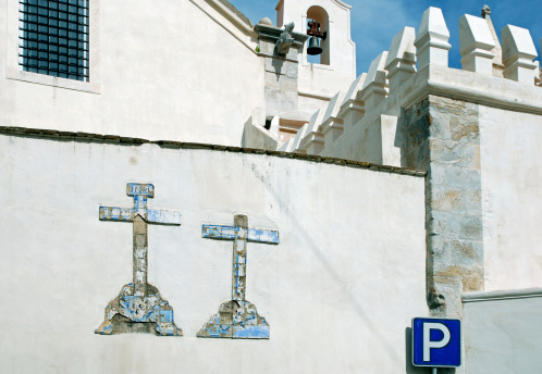 Damaged tile crosses and parking lot sign in rear of church in hilltop village of Evora, Portugal