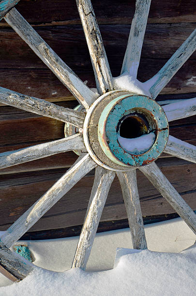 Winter Wagon Wheel A close up image of an old wooden wagon wheel in the snow. covered wagon horse cart snow winter stock pictures, royalty-free photos & images