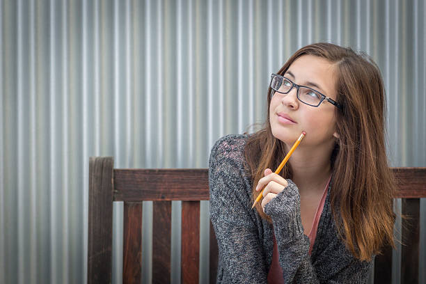 junge zum tagträumen an weibliche studentin mit stift auf der suche zur seite - teenage girls blue eyes adolescence teenager stock-fotos und bilder