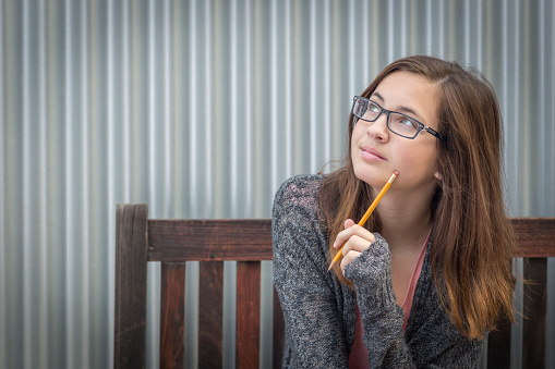 Pretty Young Daydreaming Female Student With Pencil Sitting on Bench Looking to the Side.
