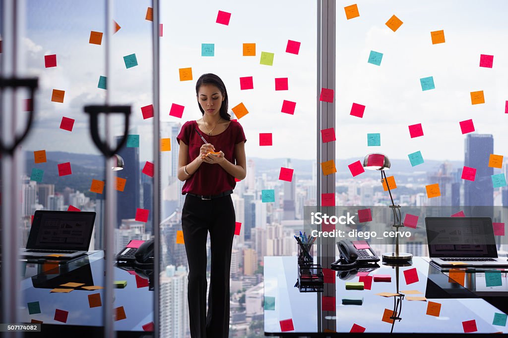 Busy Person Writing Many Sticky Notes On Large Window Mixed race secretary working in modern office in skyscraper, writing and sticking adhesive notes with tasks on window. Multi-Tasking Stock Photo