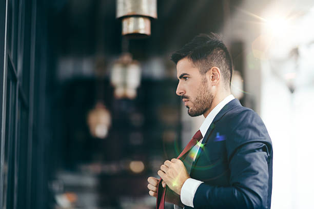 Businessman getting dressed in front of the mirror Smiling businessman fixing his necktie before going out man adjusting tie stock pictures, royalty-free photos & images