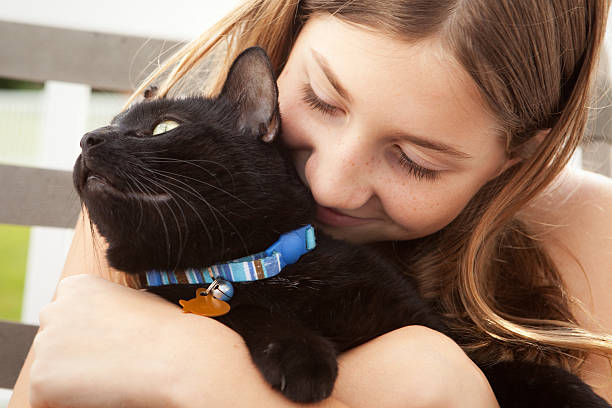 A 12 year old girl hugging her black kitty cat.