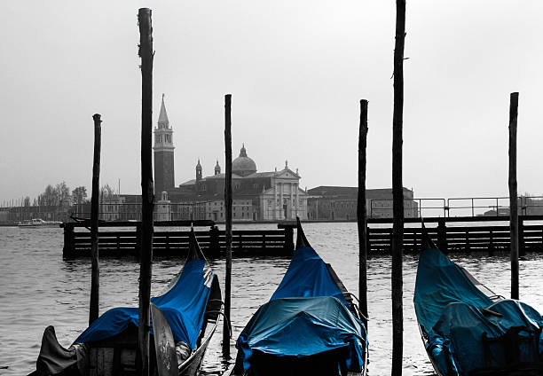 Venice canal  with a bridge in the foreground and parked moored boats and gondolas along the canalside.