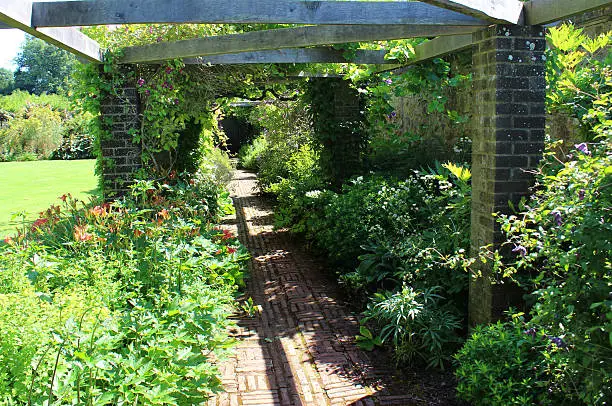 Photo showing an old block paved pathway, with weathered / aged red bricks that are full of character.  The bricks in this path have been laid out in a traditional alternating 'basketweave' pattern, while some are simply in lines, sideways and lengthways on ('stacked bond' style), defining the edges and pattern.