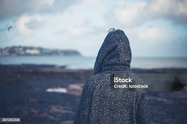 Young Woman In Hooded Coat Walking On Beach Stock Photo - Download Image Now - Sadness, Winter, Beach