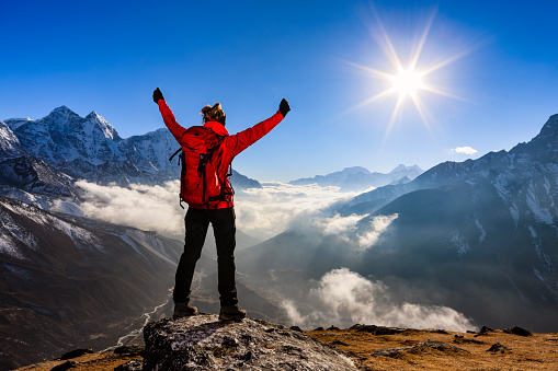 Young woman, wearing red jacket, lifts her arms in victory. She is standing on the top of a mountain and watching sunset over Himalayas .Mount Everest National Park. This is the highest national park in the world, with the entire park located above 3,000 m ( 9,700 ft). This park includes three peaks higher than 8,000 m, including Mt Everest. Therefore, most of the park area is very rugged and steep, with its terrain cut by deep rivers and glaciers. Unlike other parks in the plain areas, this park can be divided into four climate zones because of the rising altitude.http://bem.2be.pl/IS/nepal_380.jpg
