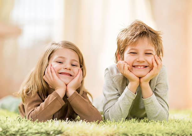 istock Smiling sibling lying on the carpet and looking at camera. 507206294