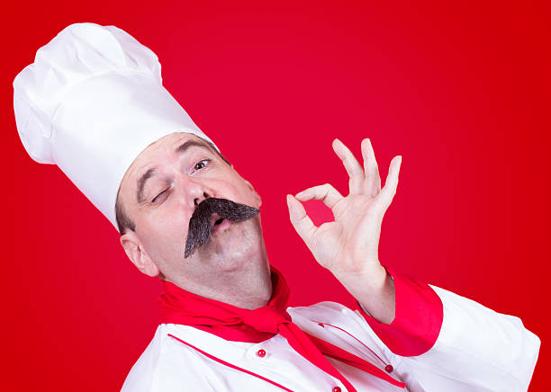 A senior chef wearing a white uniform and hat, showcasing a thoughtful expression against a vibrant yellow background. Perfect for culinary, restaurant, and promotional purposes.