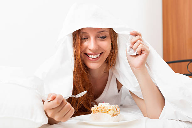 istock woman eating sweet cake under sheet in bed 507210399