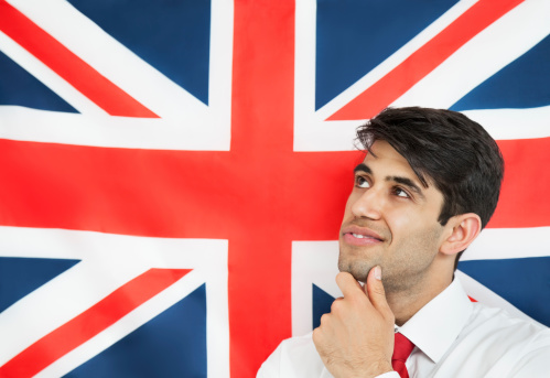 Thoughtful young man with hand on chin against British flag