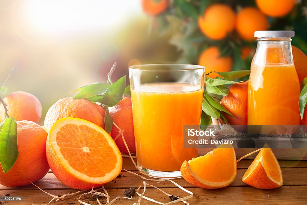 Glass of orange juice on a wooden in field Glass of orange juice on a wooden table with bottle and orange sections. Tree and field background with evening sun. Horizontal composition. Front view Juice - Drink Stock Photo