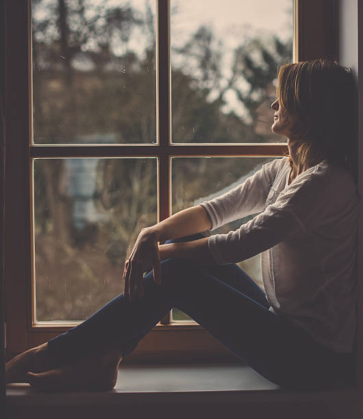 istock Young attractive woman, sitting on a window, looking outside 507214730