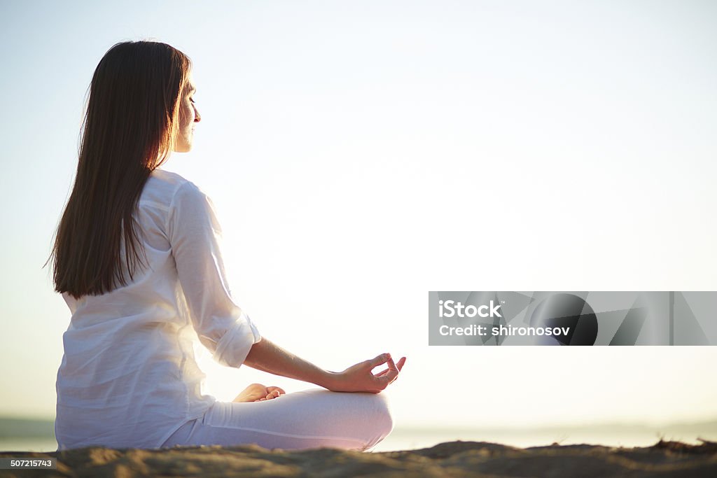 Rest and peace Side view of meditating woman sitting in pose of lotus against clear sky outdoors Adult Stock Photo