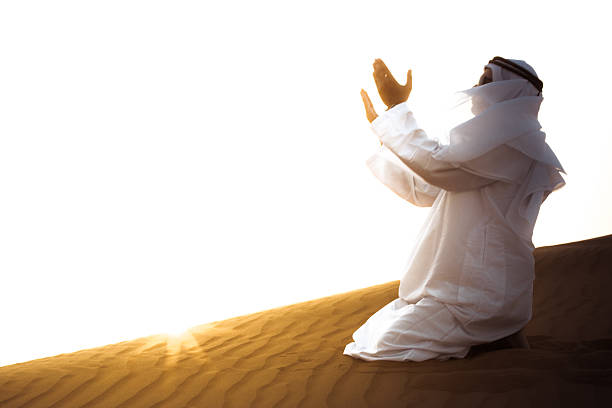 An Arab man is praying over sand dunes of Dubai, United Arab Emirates