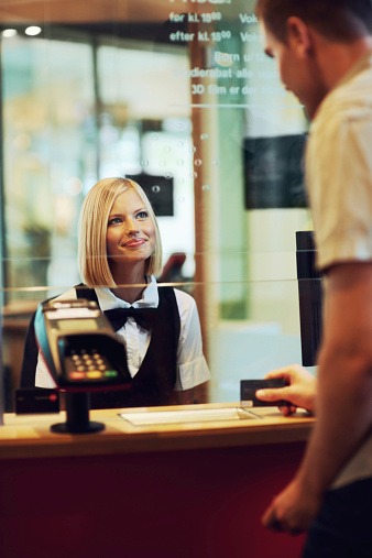 A beautiful woman dressed in uniform sitting in a ticket booth serving a male customer