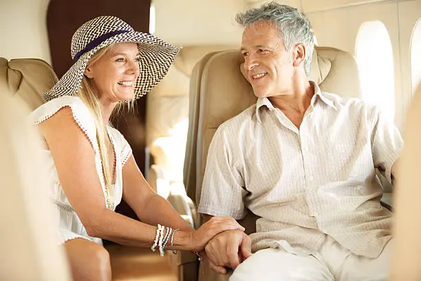 Smiling senior couple holding hands on an airplane heading overseas