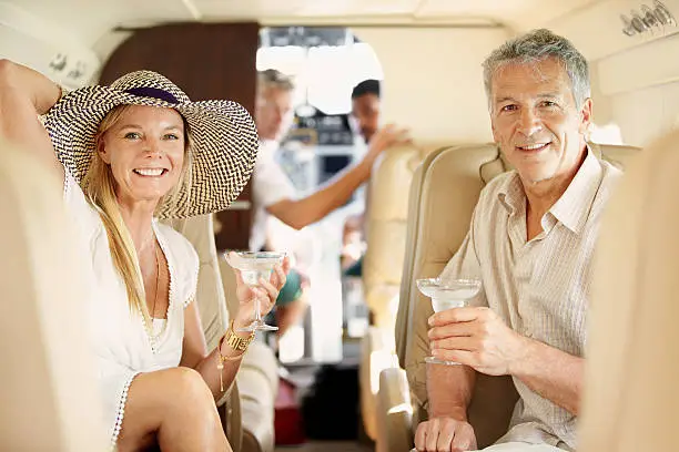 Mature couple seated in a private jet and toasting each other - portrait