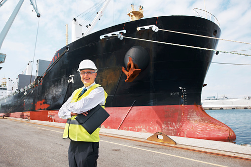 A happy foreman standing with his arms crossed in front of a ship.