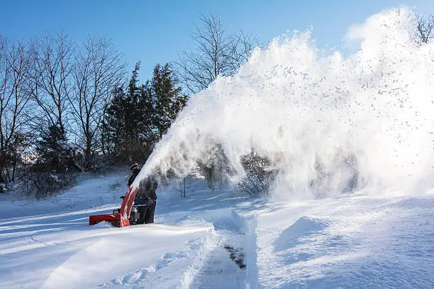 A man in black dress using a snow blower plowing snow after snow storm in the morning