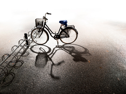 Bike with basket parked in bicycle rack with bright background and shadow on asphalt on autumn evening