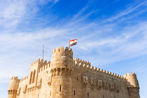 Photo of Qaitbay Castle or Citadel with Egyptian flag in Alexandria, Egypt. The Citadel of Qaitbay is a 15th-century defensive fortress on the Mediterranean coast established in 1477 AD by sultan Qaitbay