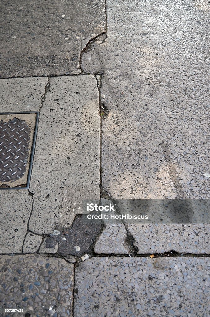 Dirty and Cracked Urban Pavement Slabs Grubby pedestrian footpath with discarded cigarettes and large cracks in the concrete surface. Asphalt Stock Photo