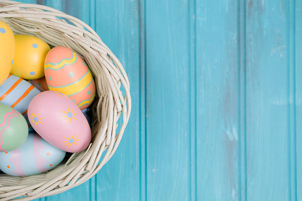 Happy Easter!  Close-up image of decorated multi-colored easter eggs lying in a white basket on a blue, vintage wooden background. Ready for an Easter Egg Hunt!   Great frame for easter and spring themes.  No people. Pastel colors.  Copyspace to right.