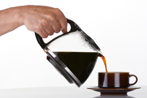 man's hand holding and pouring coffee into a brown cup